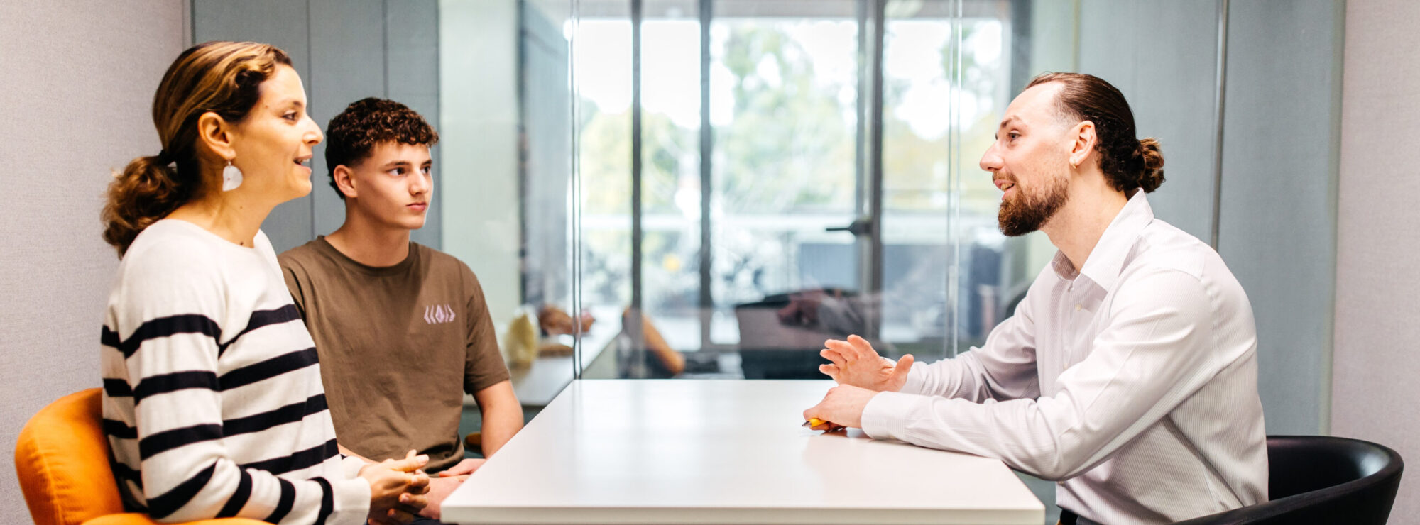 A parent and teenager sitting across from a career counsellor in a modern office, engaged in a relaxed and supportive conversation.