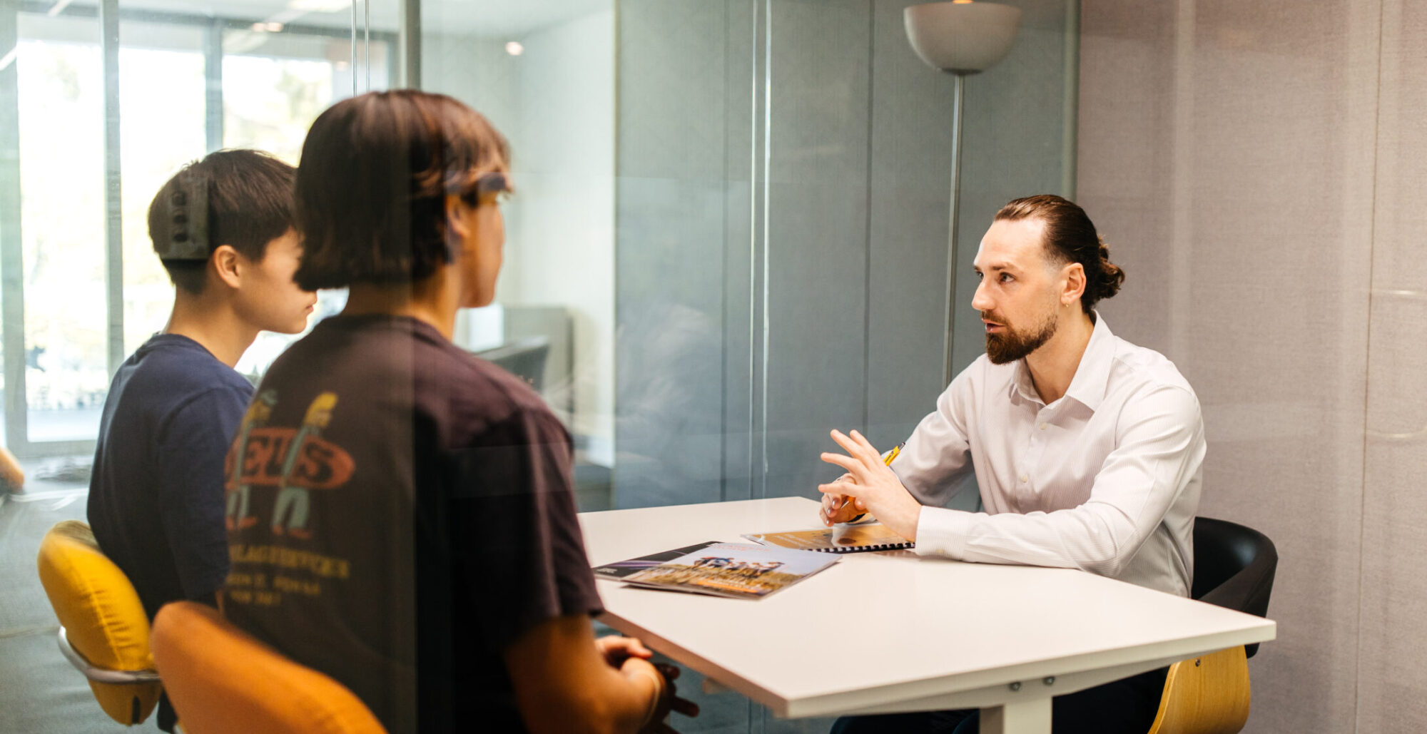 Two young people in a career counselling session with Zach James, listening attentively across a table in a modern office.