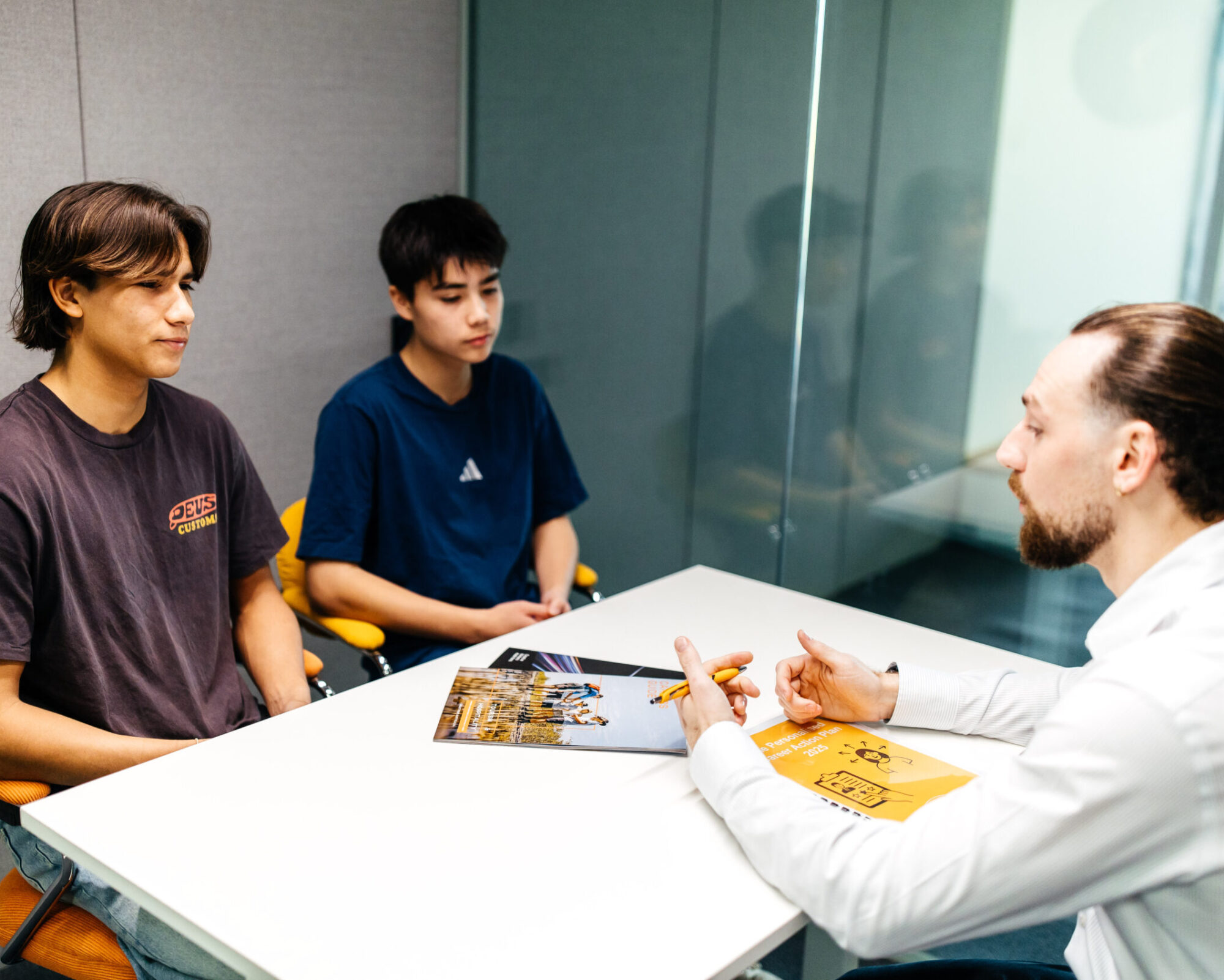 Two young men in a career counselling session with Zach James, engaged in conversation across a table in a modern office setting.